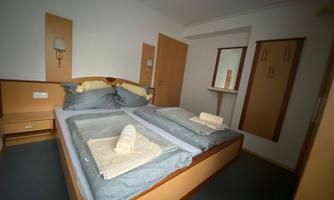 A cozy bedroom with two single beds and light wooden furniture. The walls are painted in neutral colors, and there is a mirror and a wardrobe.