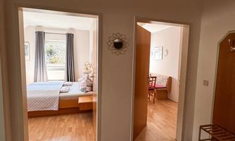 A bright hallway with two doors leading to a bedroom and a dining room. The floor is made of wood and the walls are painted light.