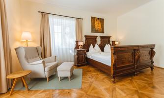A cozy bedroom with a large, antique bed and a comfortable armchair. Bright colors and a carpet create an inviting atmosphere.