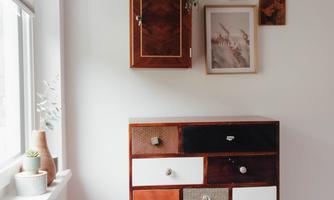 A modern dresser with colorful drawers stands against a bright wall. Above the dresser, some pictures and plants are hanging.