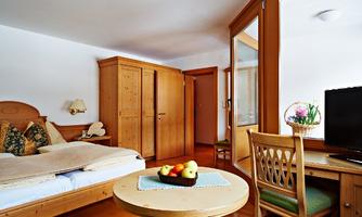 A cozy room with wooden furniture, a bed, and a table. On the table are fresh fruit and a vase of flowers.