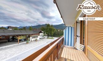 A balcony with a small table and two chairs. In the background, there are trees and mountains as well as a cloudy sky.