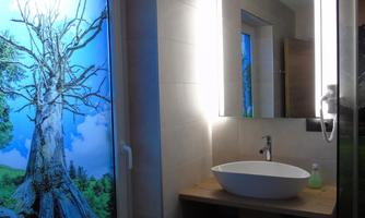A modern bathroom with a sink and a large mirror. Through the window, you can see a beautiful landscape with a tree and blue sky.