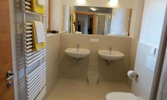 A modern bathroom with two sinks and a toilet area. The walls are bright, and there are towels and a towel radiator.