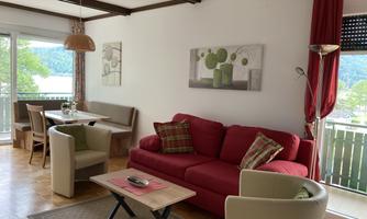 A cozy living room with a red sofa and modern furniture. Large windows offer a view of the nature outside.