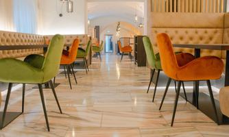 A modern restaurant with colorful chairs in green and orange. The floor is made of marble and the decor is elegant.