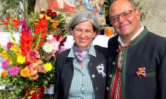 A festively decorated booth with colorful flowers and a backdrop. Two people in traditional clothing are smiling while posing in front of the booth.
