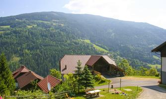 A picturesque mountain landscape with green forests and gentle hills. In the foreground, there are houses and a quiet road.