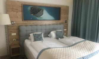 A cozy hotel room with a large bed and an elegant headboard. A picture of a tropical landscape hangs on the wall.
