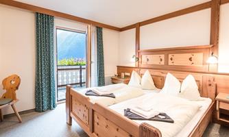 A cozy bedroom with wooden furniture and two single beds. The balcony offers a view of the beautiful mountain landscape.