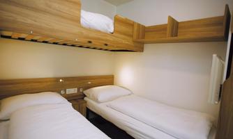 A small bedroom with a bunk bed and a single bed. The walls are light and the furniture is made of wood.