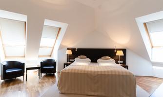 A modern bedroom with a large bed and two nightstands. Two comfortable armchairs and a slanted built-in window create a bright atmosphere.