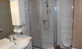 A modern bathroom with a glass shower and a sink. The walls are tiled and the decor is bright and inviting.