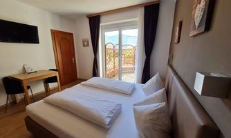 A cozy room with two beds, a table, and a television. Large windows offer a view outside.