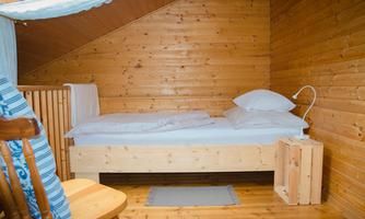A cozy room with wood paneling and a single bed. There is a wooden dresser and a comfortable chair.