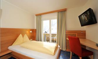 A simple, cozy room with a double bed and modern furniture. There is a desk, a television, and a balcony with a view outside.
