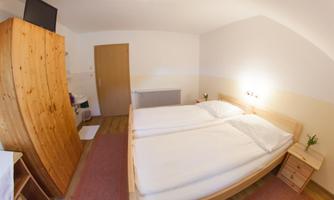 A simple room with two single beds and warm wooden furniture. There is a wardrobe, a chest of drawers, and a small table.