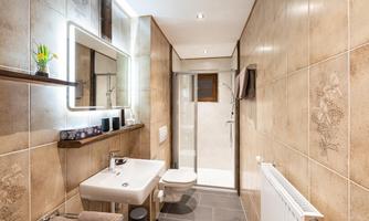 A modern bathroom with tiles and bright light. It includes a shower, a sink, and a toilet.