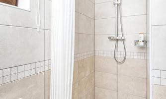A modern shower with a bright tiled floor and a white shower curtain. The walls are uniformly tiled, and there is a towel radiator.