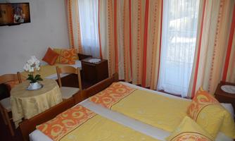 A cozy room with two beds and colorful pillows. The room has large windows, a table, and a television.
