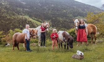 A group of children and adults stands in nature with several ponies. They enjoy the fresh air and the beautiful landscape.