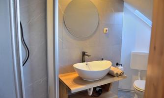 A modern bathroom with a round mirror and a stylish sink on a wooden base. The shower is in one corner, and the walls are designed in neutral colors.