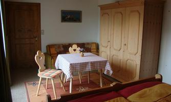 A cozy room with a table, chairs, and a bed. The room has rustic wooden decor and feels inviting.