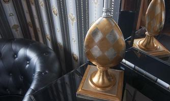 An elegant lamp with a golden and silver design stands on a black table. In the background, decorative walls with a classic pattern can be seen.