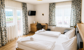 A bright and modern hotel room with two beds and large windows. The decor is simple and inviting, with a small desk and a pleasant atmosphere.