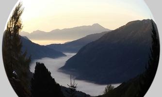 A breathtaking mountain landscape with a deep, misty gorge. The gentle hills are surrounded by trees and the sky displays a soft morning light.