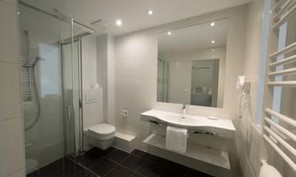 A modern bathroom with a glass shower and a large mirror. The walls are bright and the lighting is pleasant.