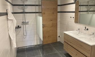 A modern bathroom with a walk-in shower and wooden details. The space is bright and generously designed.