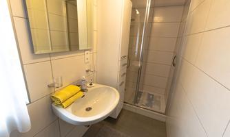 A modern bathroom with a shower and a sink. There is a large mirror and orange towels.