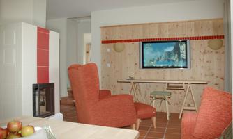 A cozy living space with red armchairs and a television on the wall. The room has a modern wood look and a fireplace.