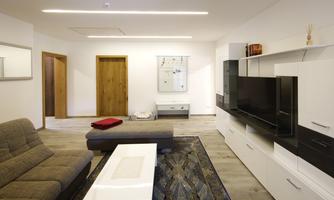 A modern living room with a gray sofa and a large television. The room has light walls and a beautiful carpet.