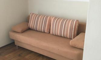 A cozy sofa with striped cushions is in a bright room. The floor is wooden and the walls are plain.