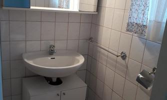 A small bathroom with white tiles and a sink. There is a mirror and a radiator, as well as a curtain next to the window.