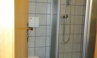 A bathroom with a shower and a toilet. There are tiles and a blue towel on the floor.
