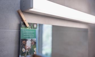 A bathroom with a mirror and a light above it. A note with a picture of a cow and information is hanging on the mirror.