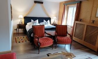 A cozy bedroom with a large bed and two red armchairs. The warm wood paneling and soft light create an inviting atmosphere.