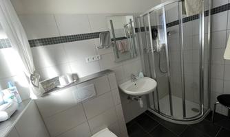 A modern bathroom with a shower, sink, and toilet. The walls are brightly tiled and there are windows for natural light.
