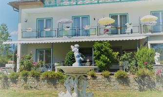 A charming house with a balcony and colorful umbrellas. In the foreground, there is a decorative fountain with sculptures.