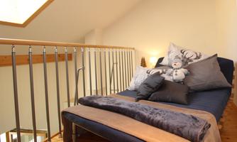 A cozy sleeping area with a sofa, cushions, and a plush toy. The bright atmosphere is enhanced by the large window and the wooden details.