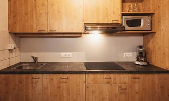 A modern kitchen with wooden cabinets and a dark countertop. There is a sink, a stove, and a microwave.