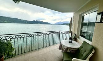 A beautiful balcony with a view of a lake and surrounding mountains. There is a table and chairs, perfect for relaxing hours outdoors.
