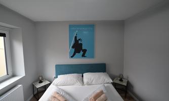 A modern bedroom with a blue headboard and a painting on the wall. On the bed are two towels and two nightstands with lamps.