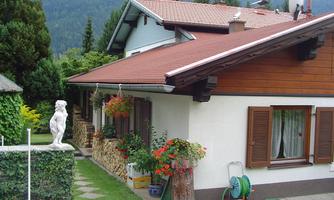 A beautiful house with a red roof and blooming plants in the garden. In the background, mountains and a clear sky can be seen.