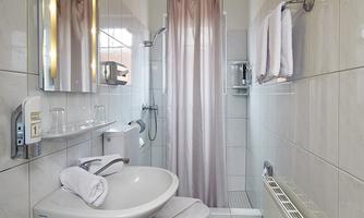 A modern bathroom with white tiles and a sink. Curtains and towels create an inviting look.