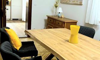 A cozy dining area with a large wooden table and black chairs. A yellow vase sits on the table, and the walls are decorated with artworks.