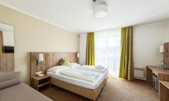 A modern bedroom with two beds and cozy furnishings. Large windows with curtains provide plenty of daylight.